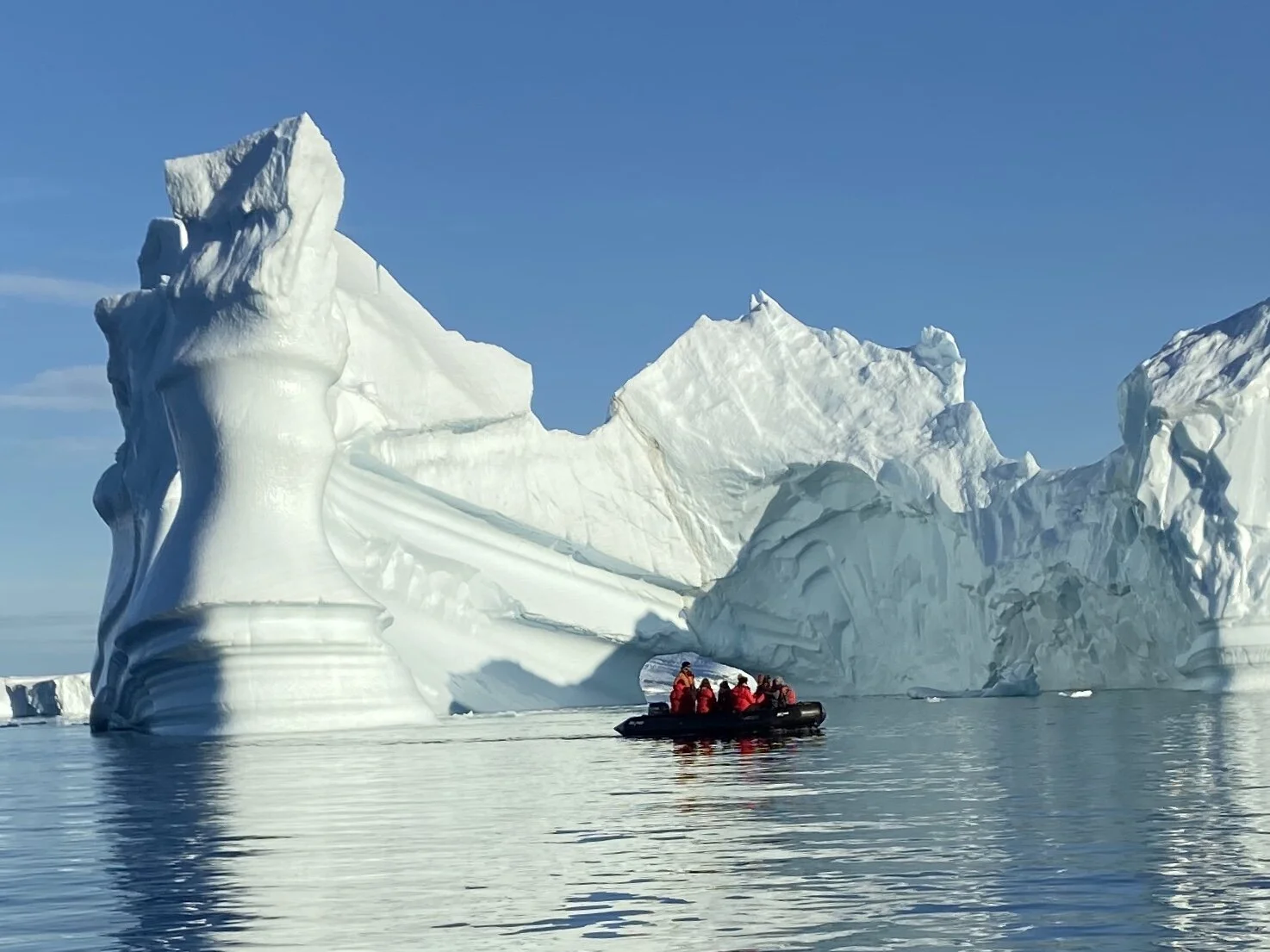 Group in a small Zodiac boat exploring towering icebergs in calm Antarctic waters.