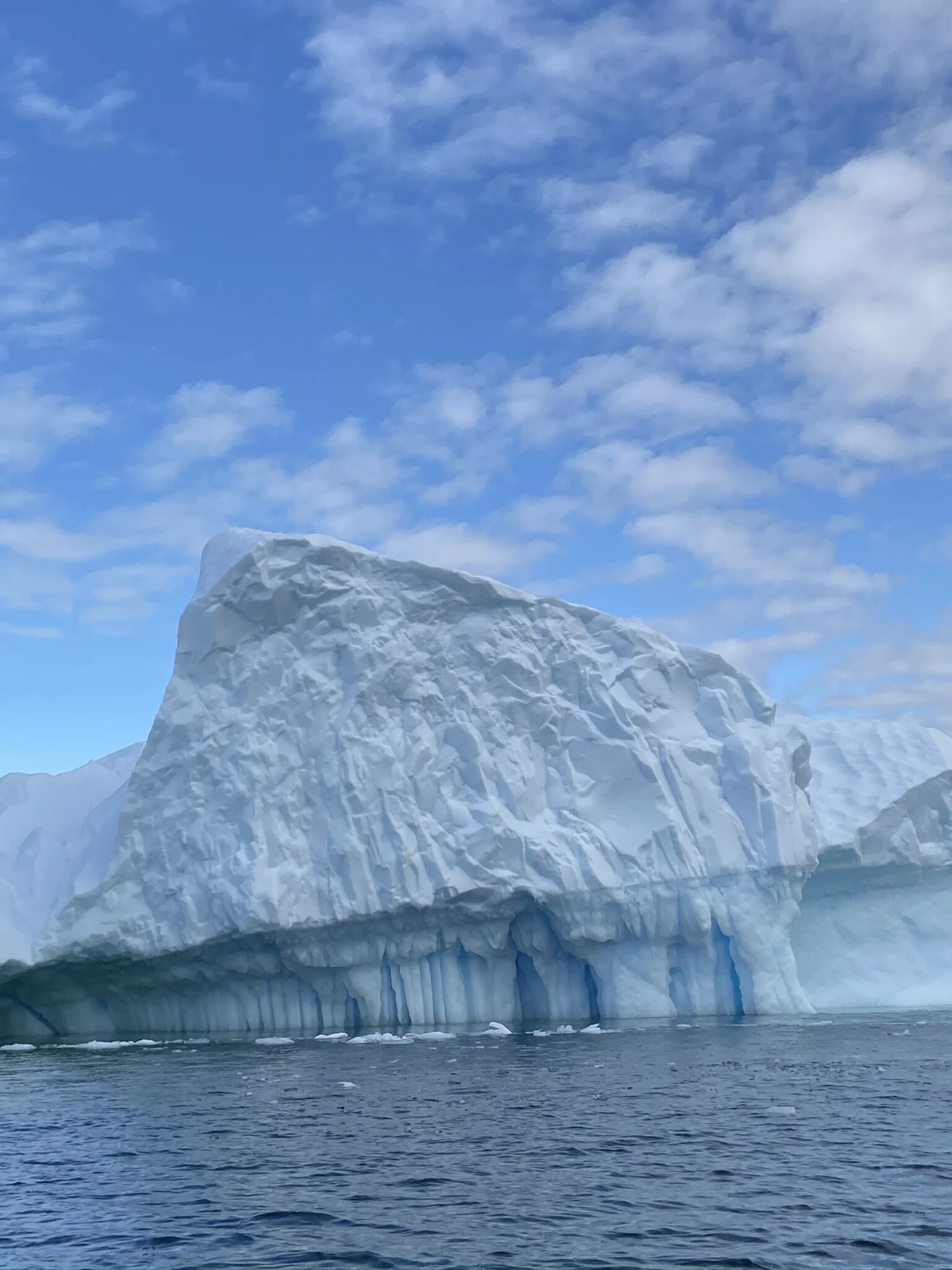 Massive iceberg with blue streaks rising above the Antarctic ocean under a partly cloudy sky