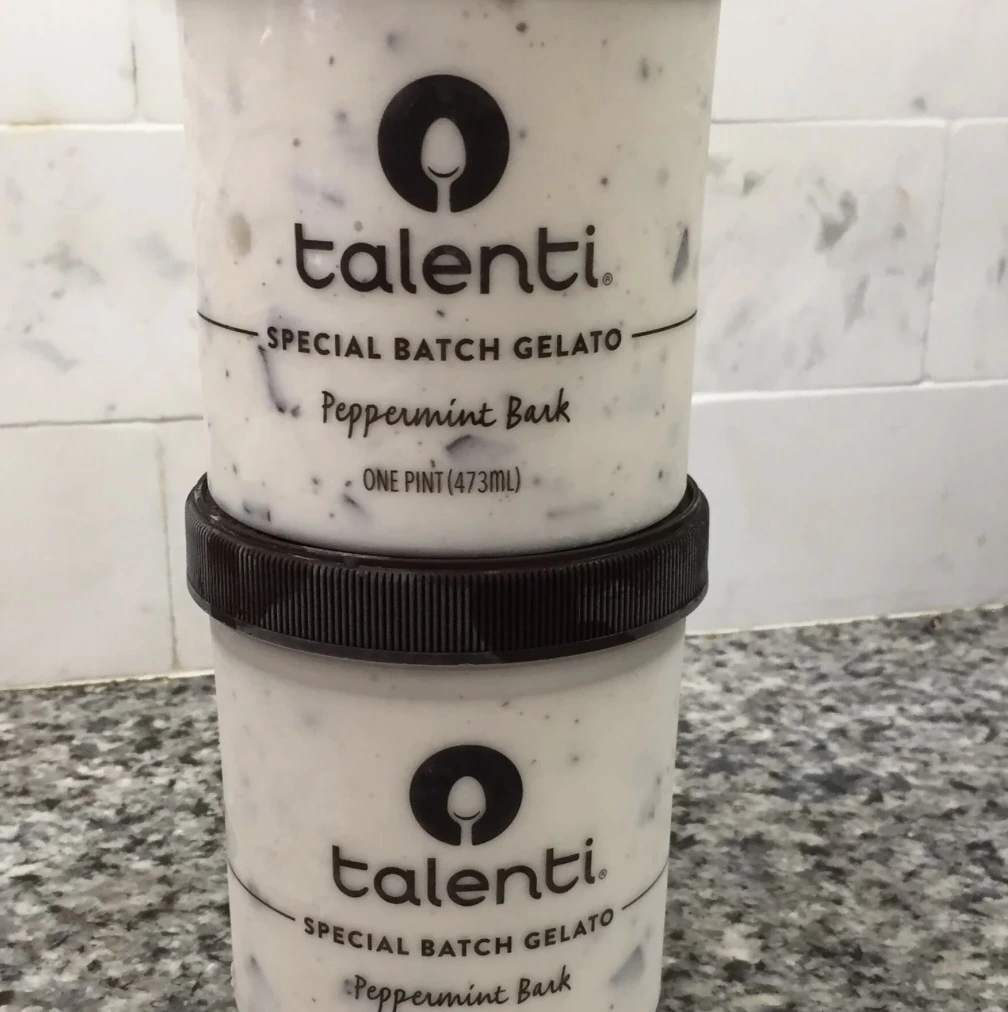 Two stacked pints of Talenti Special Batch Gelato in the Peppermint Bark flavor, placed on a speckled granite countertop with a white tiled backsplash.