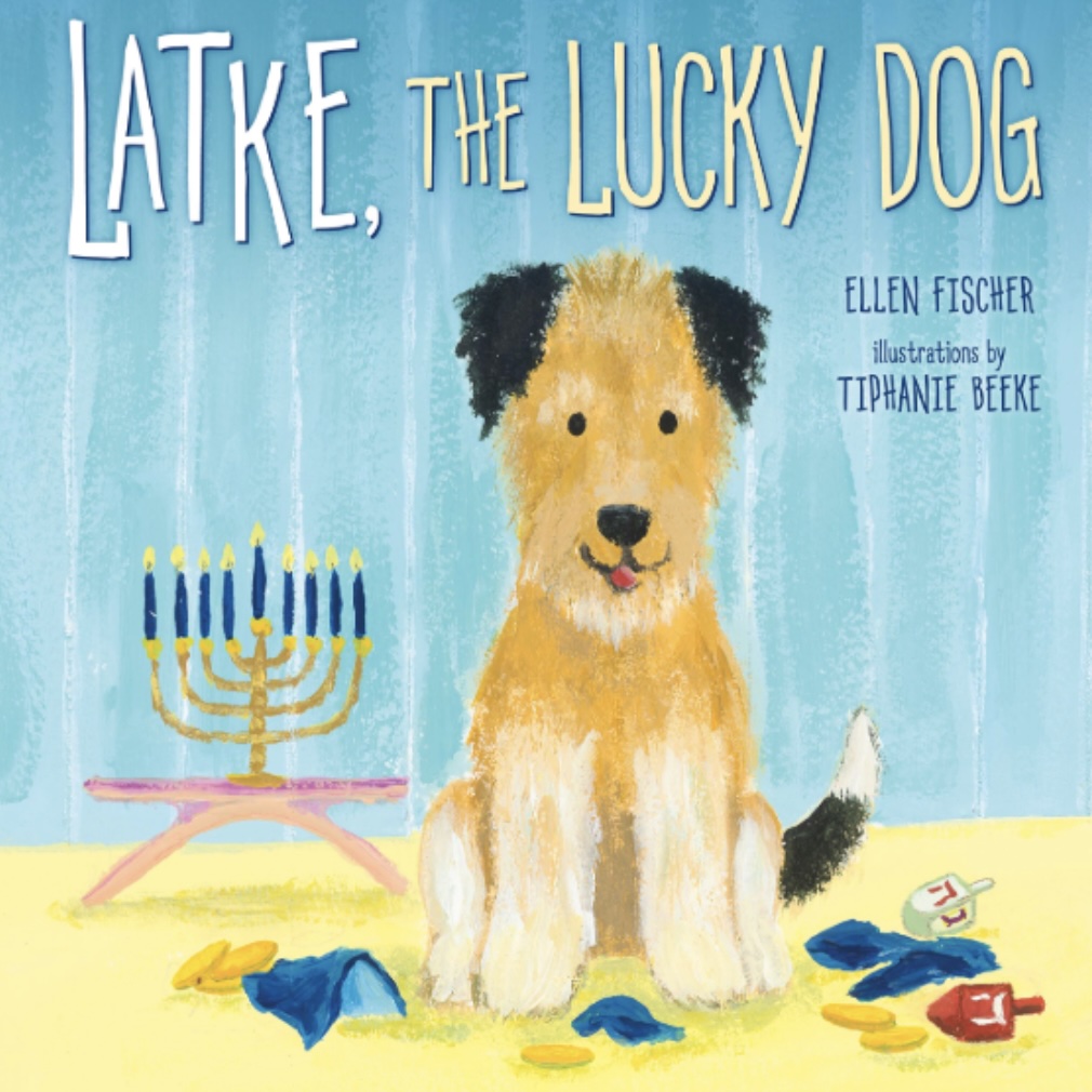 Illustrated book cover of Latke, the Lucky Dog by Ellen Fischer, with illustrations by Tiphanie Beeke. The cover shows a cheerful brown and white dog sitting on the floor surrounded by dreidels and gold coins, with a lit menorah in the background.