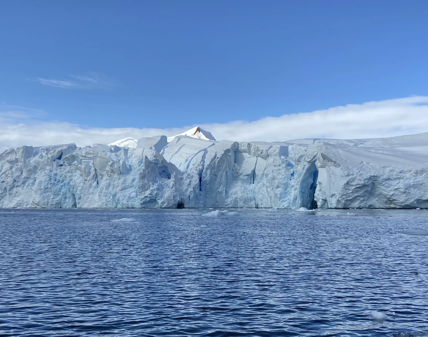 Expansive Antarctic glacier with jagged ice cliffs, calm blue water, and a clear sky