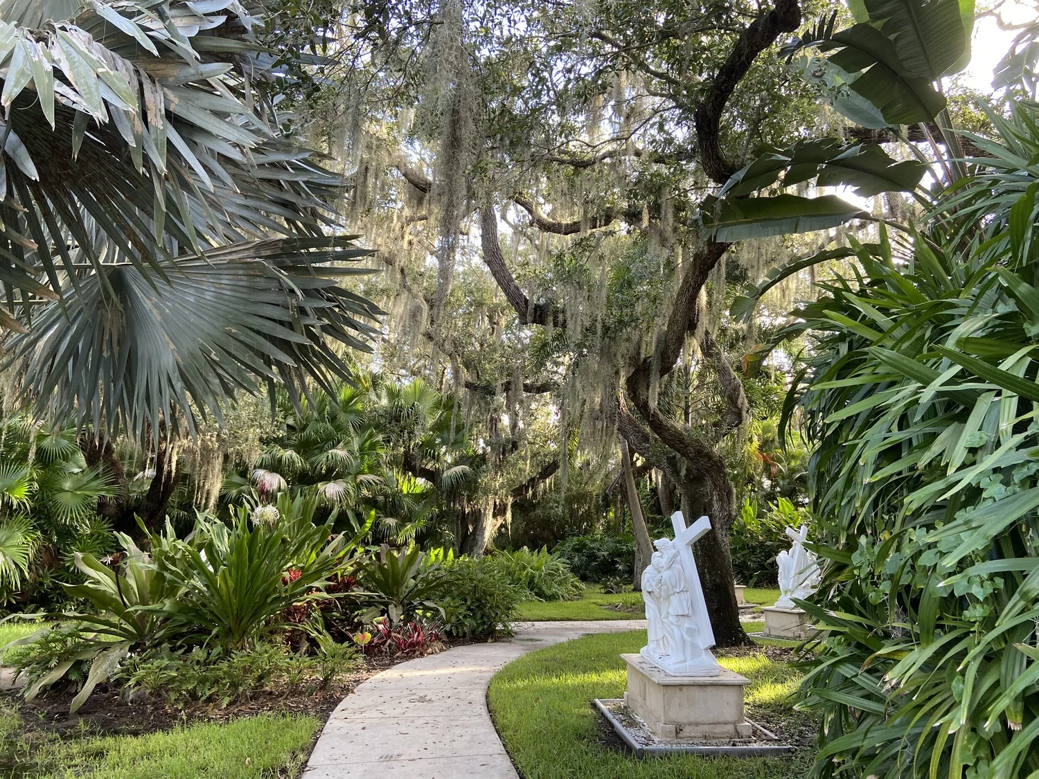 Peaceful garden path lined with lush tropical plants and statues, creating a serene retreat atmosphere